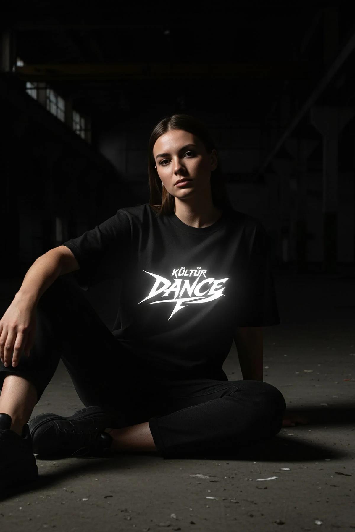 KÜLTÜR DANCE reflektörlü ön baskılı siyah oversize tişört, model üzerinde karanlık arka planda