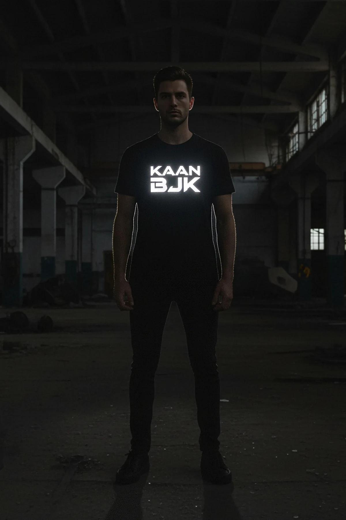 KAAN BJK reflektör baskılı siyah tişört — model tam cepheden, ışıkta parlayan ön baskı görünümü
