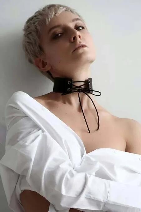 Black faux leather wide lace-up choker collar with metal grommets and dangling dark rope ties worn on neck