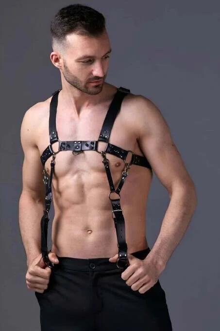 Black faux leather adjustable chest harness with gold-tone O-ring hardware worn by man over bare torso